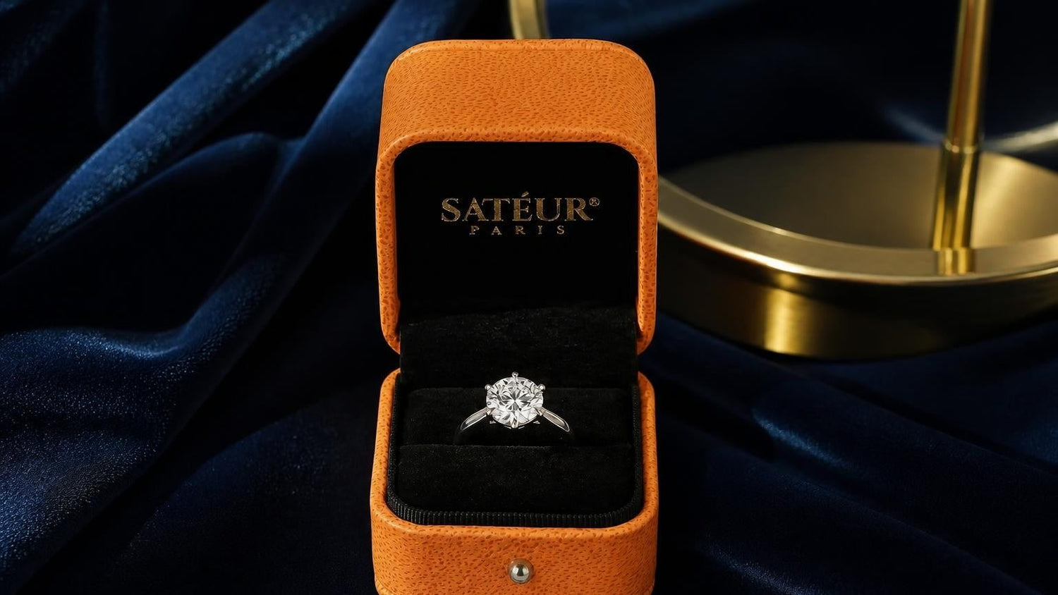 Diamond simulant ring in open orange Satéur box on deep-navy velvet — diamond vs cubic zirconia comparison