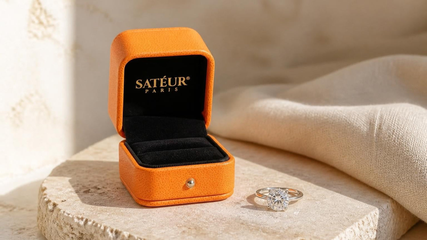 Satéur moissanite ring on pale travertine with open Satéur ring box
