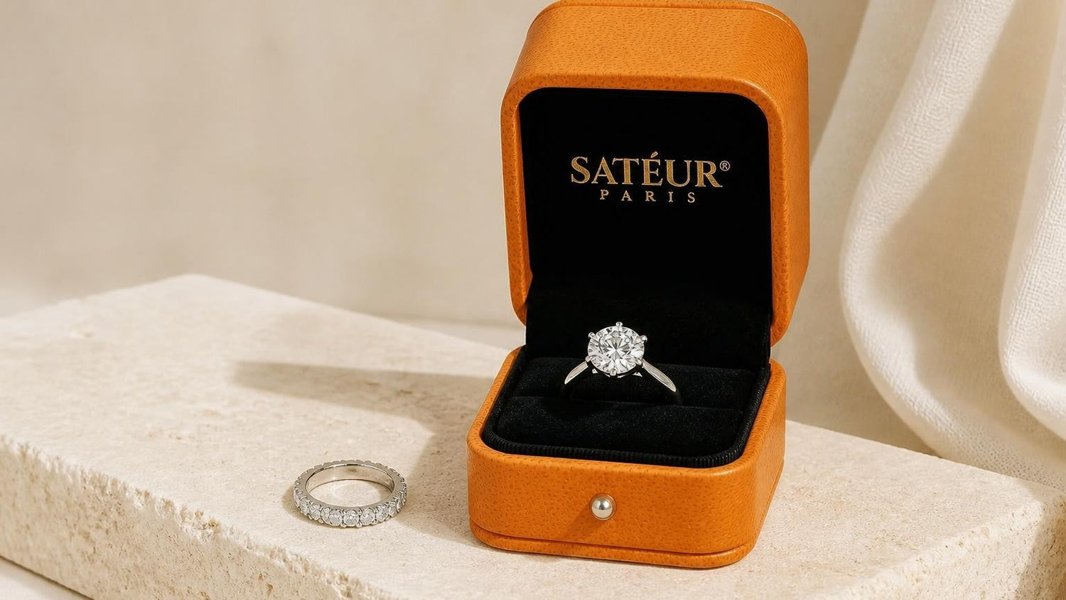 White sapphire engagement ring beside Satéur Destinée Ring in open orange box