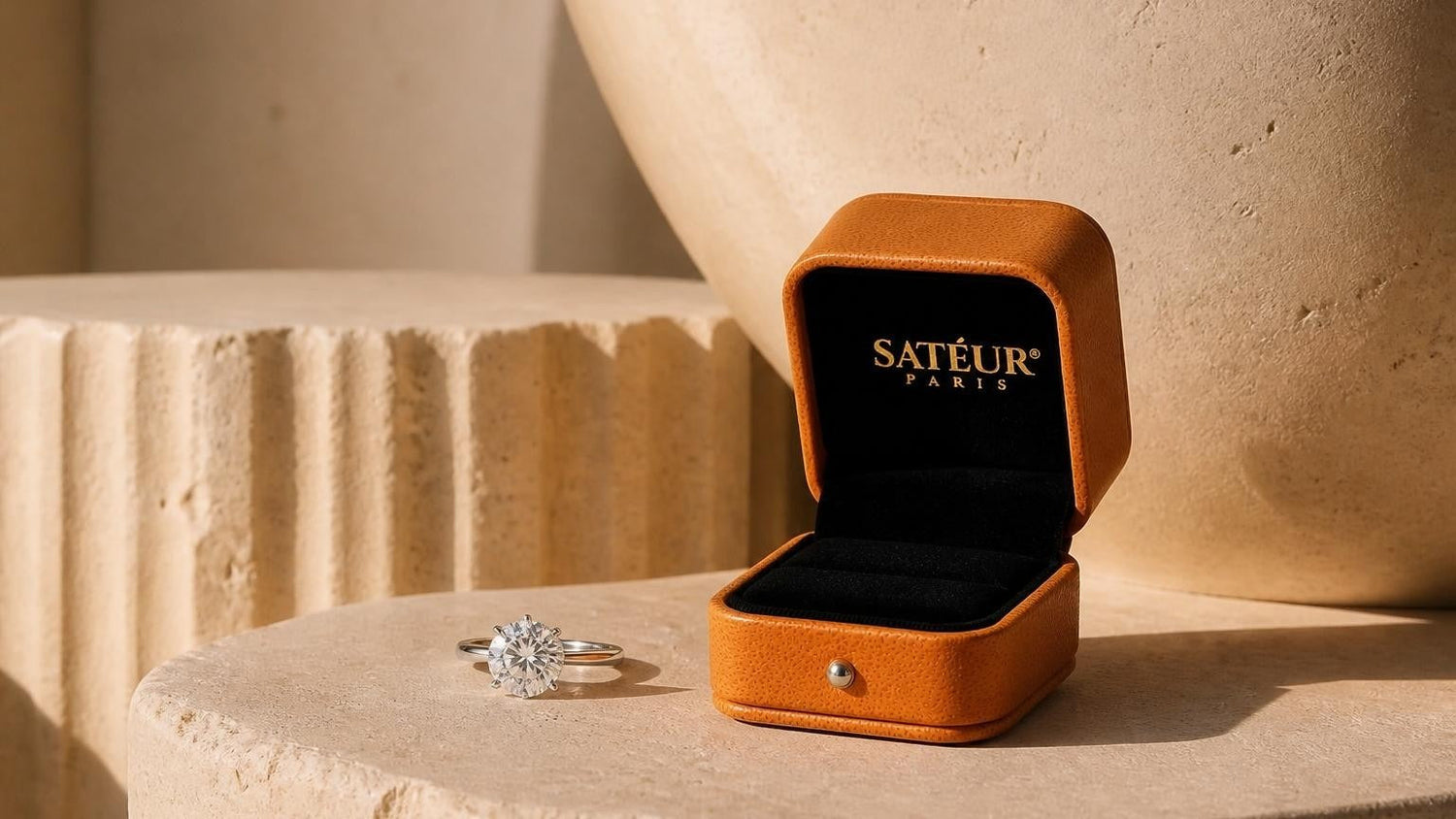 A widow's light ring resting on a stone plinth with an open orange Satéur box