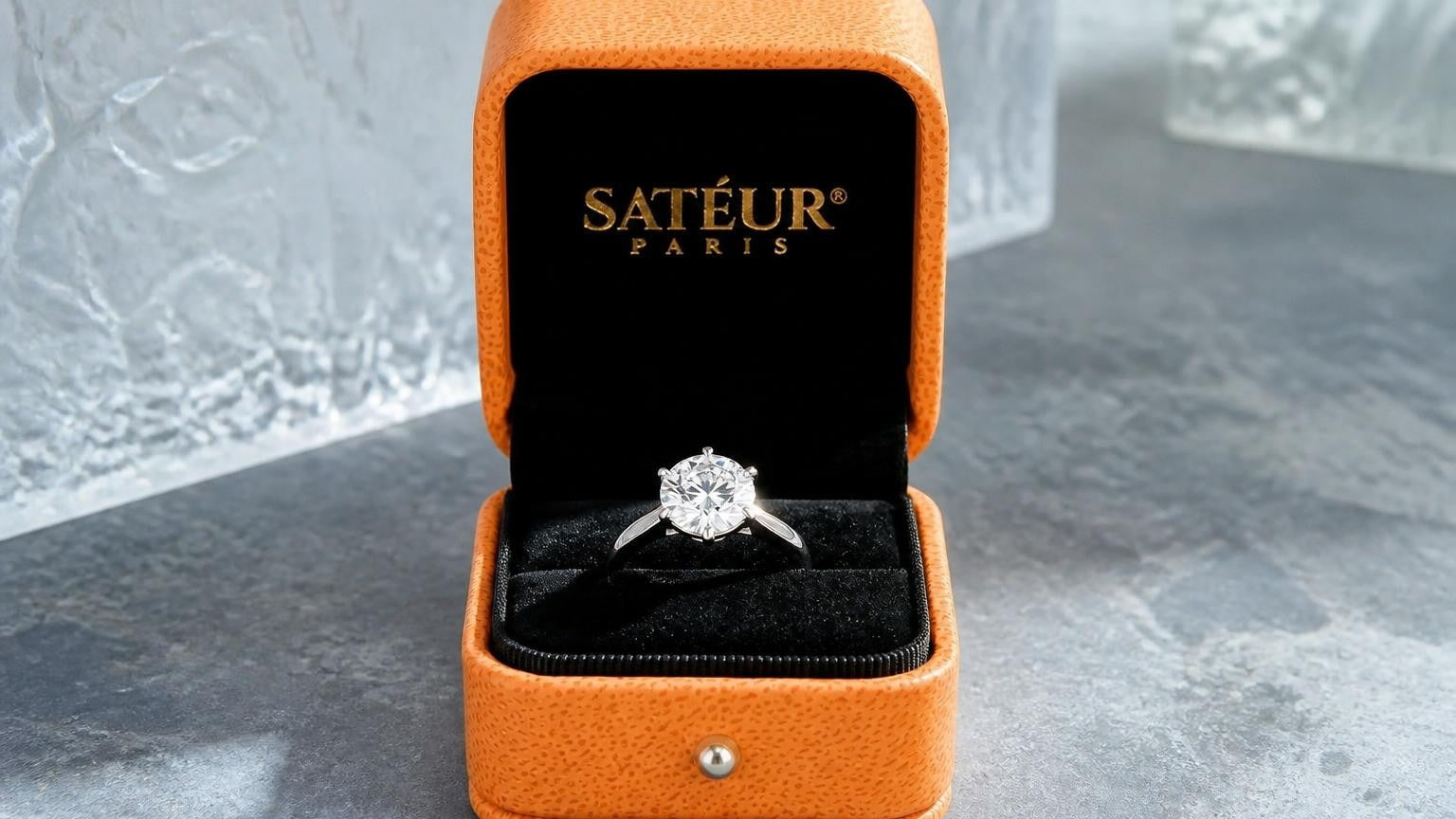 Satéur diamond simulant ring in open orange Satéur box showing SATÉUR PARIS gold wordmark on black velvet interior